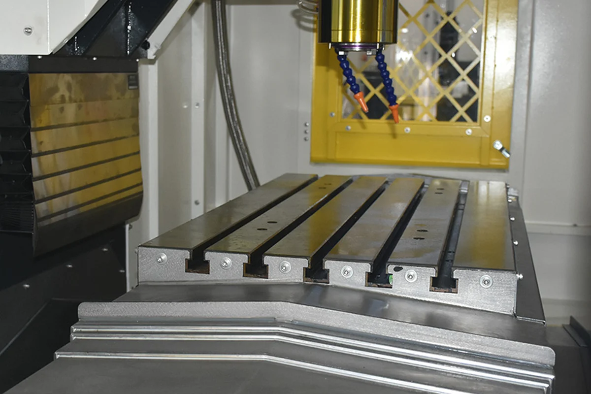 Spindle nose and coolant nozzles above a slotted machine table inside a vertical machining center
